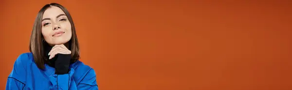Femme coûteuse avec nez percé regardant la caméra tout en pensant sur fond orange, bannière — Photo de stock