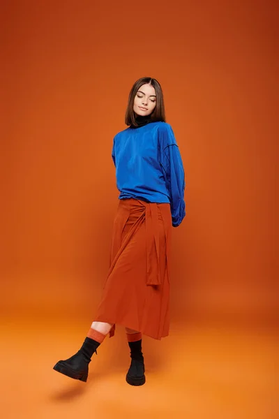 Outono traje temporada, mulher atraente na saia e camisola azul em pé no pano de fundo laranja — Fotografia de Stock