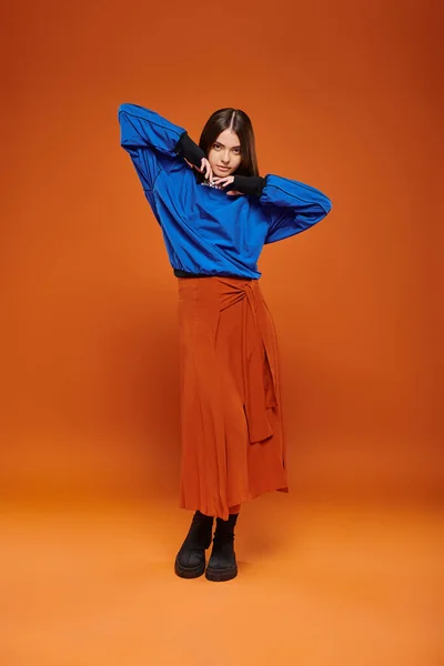 Mode d'automne, jolie femme en jupe, sweat-shirt bleu et bottes debout sur fond orange — Stock Photo