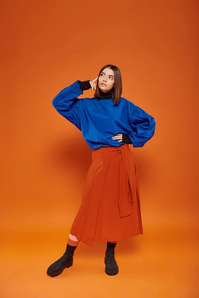 Pensive young woman with pierced nose standing in autumn attire with hand on hip on orange backdrop — Stock Photo