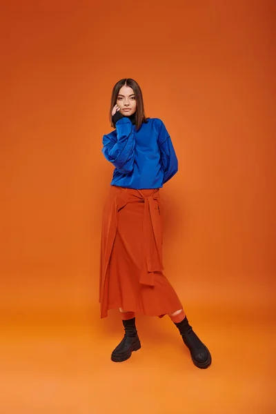 Fashionable and young woman with pierced nose standing in autumn attire on orange background — Stock Photo