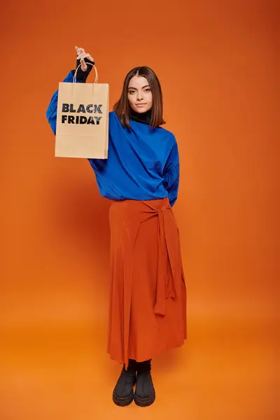 Mujer joven de moda en traje de otoño y botas con bolsa de compras con letras de viernes negro - foto de stock