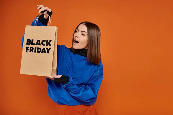 Mujer joven sorprendida en traje de otoño mirando el bolso de compras con letras de viernes negro en naranja - foto de stock