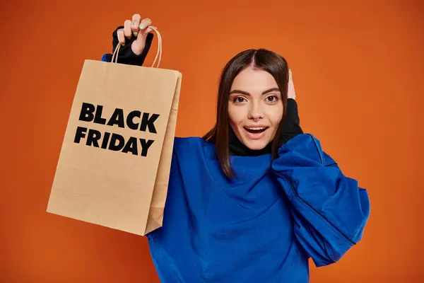 Mujer joven excitada en traje de otoño sosteniendo bolsa de compras con letras de viernes negro en naranja - foto de stock