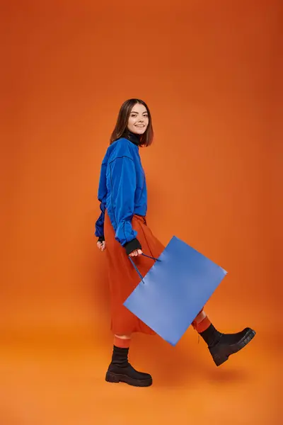 Щаслива жінка в осінньому вбранні, що йде з сумкою на помаранчевому тлі, концепція чорної п'ятниці — стокове фото