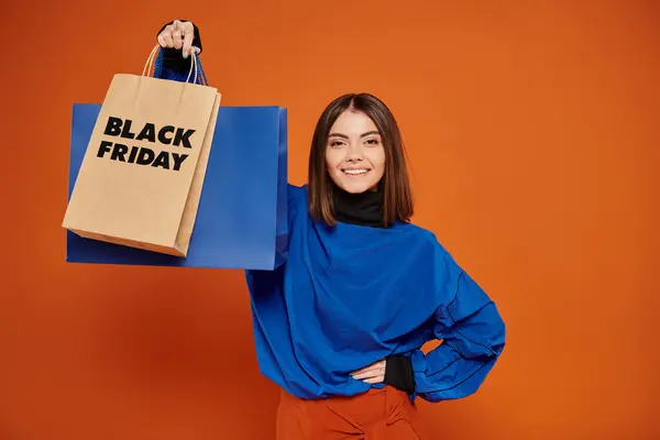 Joyful woman in autumn outfit standing with shopping bags on orange backdrop, black friday concept — Stock Photo