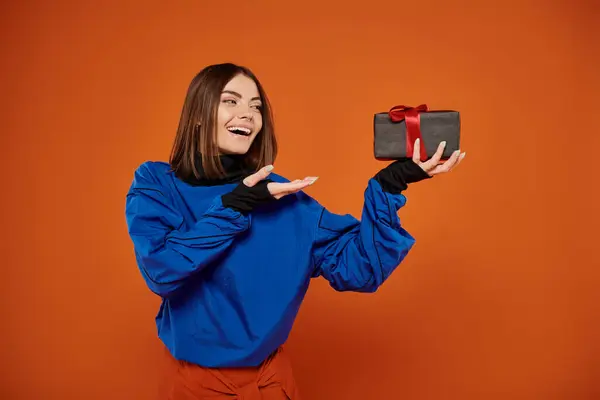 Happy woman with short brunette hair pointing at wrapped present on orange backdrop, black friday — Stock Photo