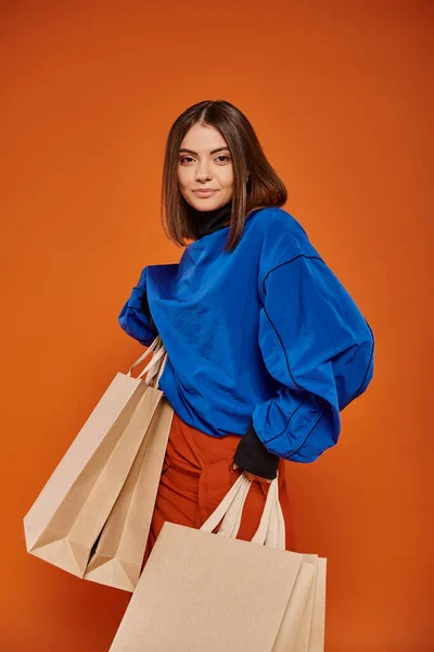 Smiling woman holding shopping bags and standing on orange backdrop, black friday sales concept — Stock Photo