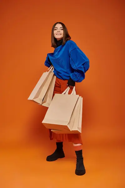 Mulher animado segurando sacos de compras e de pé em pano de fundo laranja, preto conceito de vendas sexta-feira — Fotografia de Stock