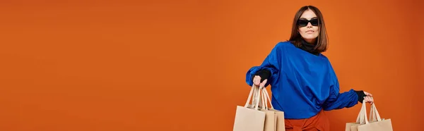 Hermosa mujer en gafas de sol con estilo sosteniendo bolsas de compras sobre fondo naranja, bandera de viernes negro - foto de stock