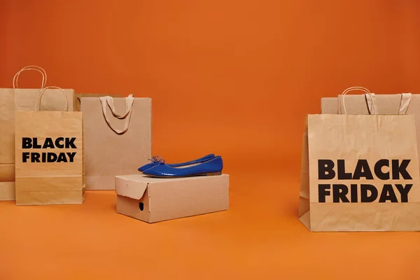 Ballet pisos en caja de cartón cerca de bolsas de compras con letras de viernes negro sobre fondo naranja - foto de stock
