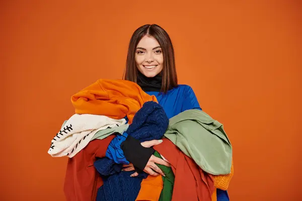 Joyeuse jeune femme aux cheveux bruns tenant des vêtements automnaux colorés, concept du vendredi noir — Photo de stock