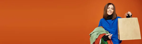 Banner of happy woman holding pile of colorful autumnal clothes and shopping bag on black friday — Stock Photo