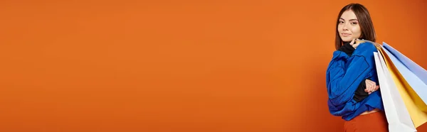 Bannière de femme positive en vêtements automnaux tenant des sacs à provisions le vendredi noir, fond orange — Photo de stock