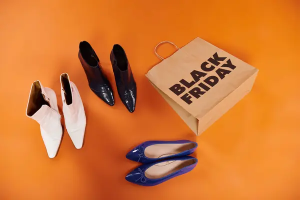 Автентичні чоботи та плоске взуття біля торгової сумки з чорними п'ятничними літерами на апельсині, вид зверху — стокове фото