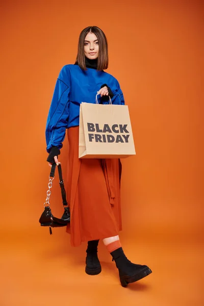 Young woman in autumnal clothes standing with trendy handbag and shopping bag on black friday — Stock Photo