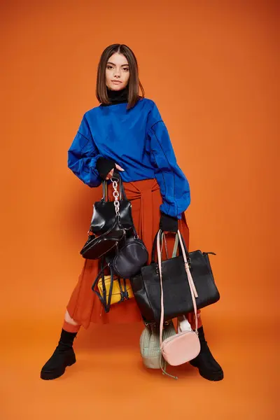 Mujer joven en ropa otoñal sosteniendo diferentes bolsas sobre fondo naranja, concepto de viernes negro - foto de stock