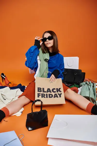 Elegante donna in occhiali da sole seduto intorno a borse e vestiti caldi con nero venerdì shopping bags — Foto stock