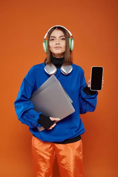 Jeune femme en casque et tenue automnale tenant smartphone et ordinateur portable, cyber lundi — Photo de stock
