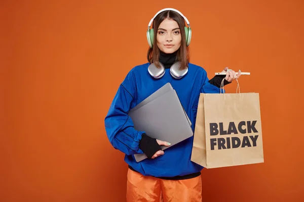 Young woman in headphones and autumnal outfit holding gadgets and shopping bag, black monday — Stock Photo