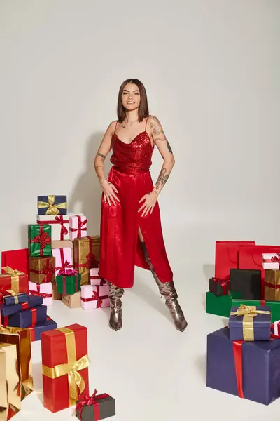 Jovem alegre em vestido vermelho de pé perto embrulhado presentes de Natal em pano de fundo cinza — Fotografia de Stock