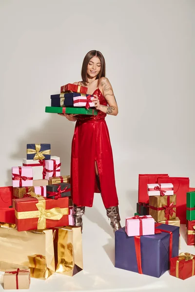 Femme brune élégante en robe tendance tenant des cadeaux et les regardant, concept de cadeaux de vacances — Photo de stock