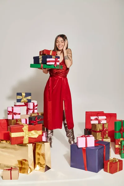 Erstaunt glückliche Frau im roten Kleid, die schockiert und lächelnd auf Geschenke schaut, Urlaubs-Geschenkkonzept — Stockfoto