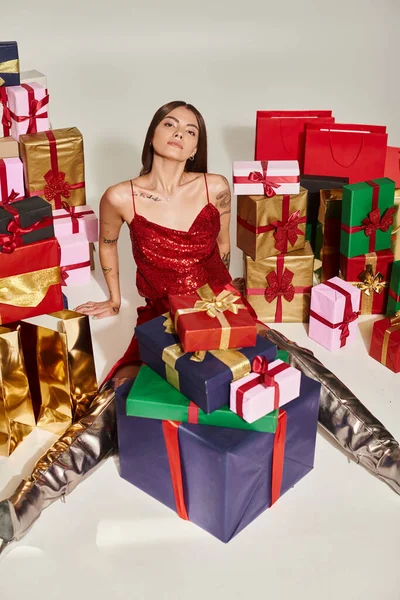 Beautiful woman in festive attire surrounded by presents looking at camera, holiday gifts concept — Stock Photo