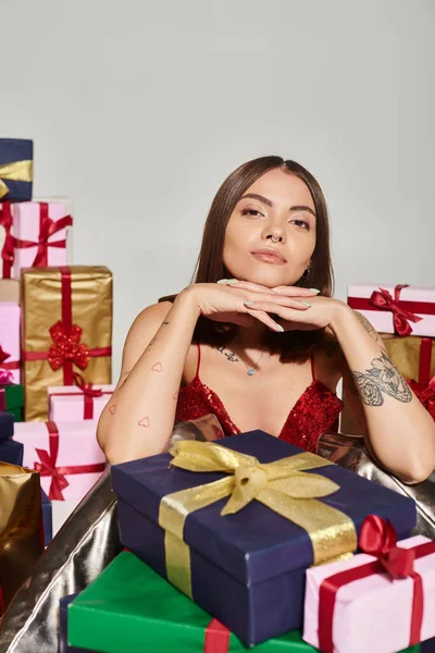 Beautiful woman with tattoos and pierced nose posing with hands under chin, holiday gifts concept — Stock Photo