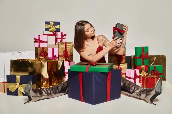 Attractive young woman with tattoos in festive attire sitting and looking at present, holiday gifts — Stock Photo