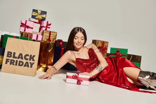 Cheerful young lady lying on floor surrounded by presents on ecru background, black friday concept — Stock Photo