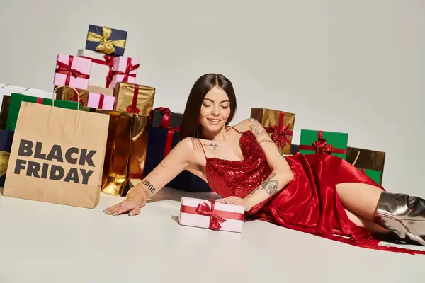 Joyeuse jeune femme couchée sur le sol entouré de cadeaux sur fond écru, concept du vendredi noir — Photo de stock