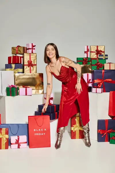 Senhora atraente em vestido vermelho inclinando-se para a frente para pegar saco de compras vermelho, conceito de sexta-feira preta — Fotografia de Stock