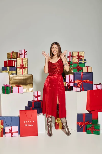 Happy young lady in red dress with tattoos gesturing and smiling at camera, black friday concept — Stock Photo