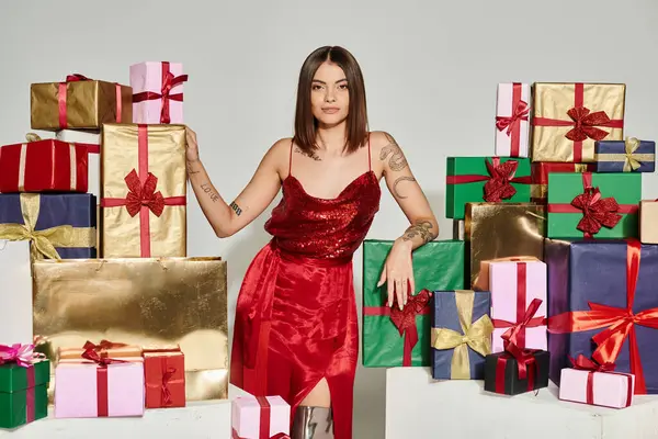 Молода жінка в червоній сукні стоїть поруч з подарунками, дивлячись на камеру, концепція святкових подарунків — стокове фото