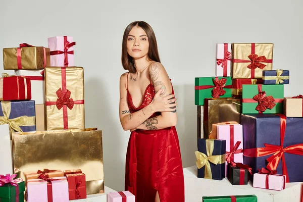 Jolly female model in red dress with crossed arms standing next to presents, holiday gifts concept — Stock Photo