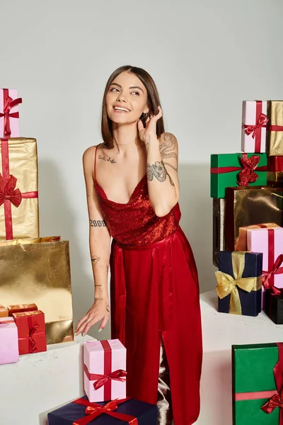Jeune femme rêveuse en robe rouge avec la main derrière l'oreille détournant les yeux, concept de cadeaux de vacances — Photo de stock