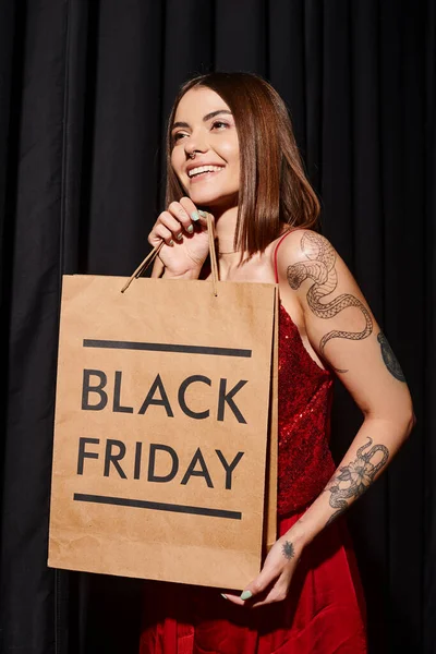 Cheerful woman with shopping bag in hands with black curtains on backdrop, black friday — Stock Photo