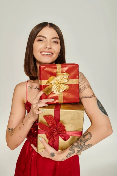 Mulher alegre atraente segurando pilha de presentes e sorrindo para a câmera, conceito de presentes de férias — Fotografia de Stock