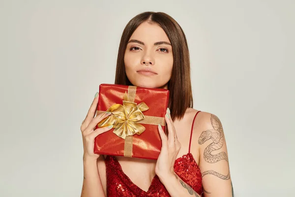 Мечтательная молодая женщина держит красный подарок и смотрит прямо в камеру, праздничные подарки концепции — стоковое фото
