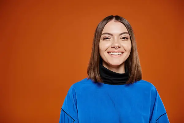 Atractiva mujer sonriente en chaqueta azul casual sonriendo alegremente a la cámara sobre fondo naranja - foto de stock