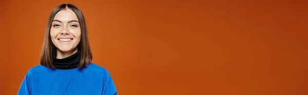 Beautiful woman with pierced nose in casual blue jacket smiling at camera on orange backdrop, banner — Stock Photo