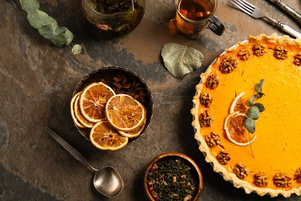 Natura morta del Ringraziamento, torta di zucca guarnita vicino a fette di arancia essiccate e spezie sulla superficie di pietra — Foto stock