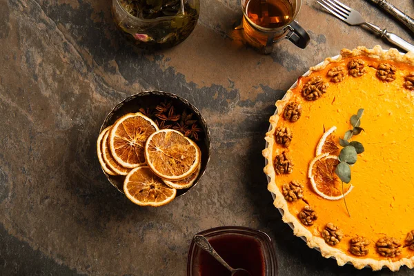 Thanksgiving pumpkin pie with walnuts and orange slices near warm tea and spices on textured surface — Stock Photo