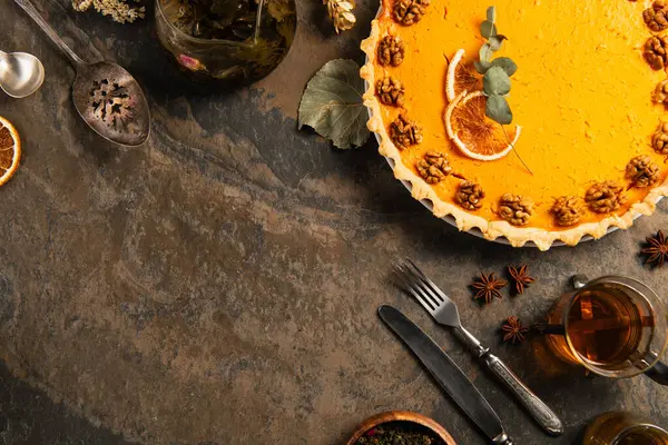 Délicieuse tarte à la citrouille avec tranches d'orange et noix près de couverts vintage et thé chaud sur table en pierre — Photo de stock