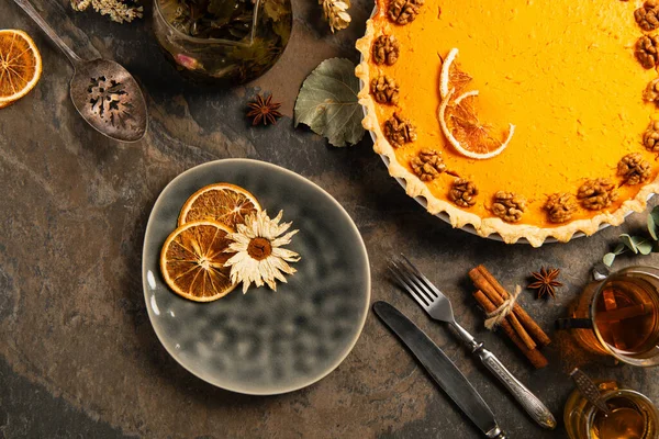 Thanksgiving backdrop, decorated pumpkin pie near cutlery, tea and spices with herbs on stone table — Stock Photo