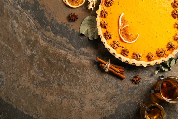 Fondo de acción de gracias, pastel de calabaza con nueces y rodajas de naranja cerca de palitos de canela y té caliente - foto de stock