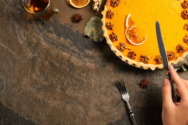 Cropped view of male hand with knife near garnished thanksgiving pie and hot tea on stone tabletop — Stock Photo