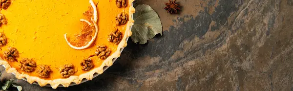 Thanksgiving treat, homemade pumpkin pie with walnuts and orange slices on stone backdrop, banner — Stock Photo