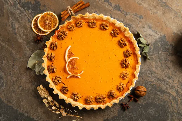 Thanksgiving setting, pumpkin pie with walnuts and orange slices near cinnamon sticks on stone table — Stock Photo